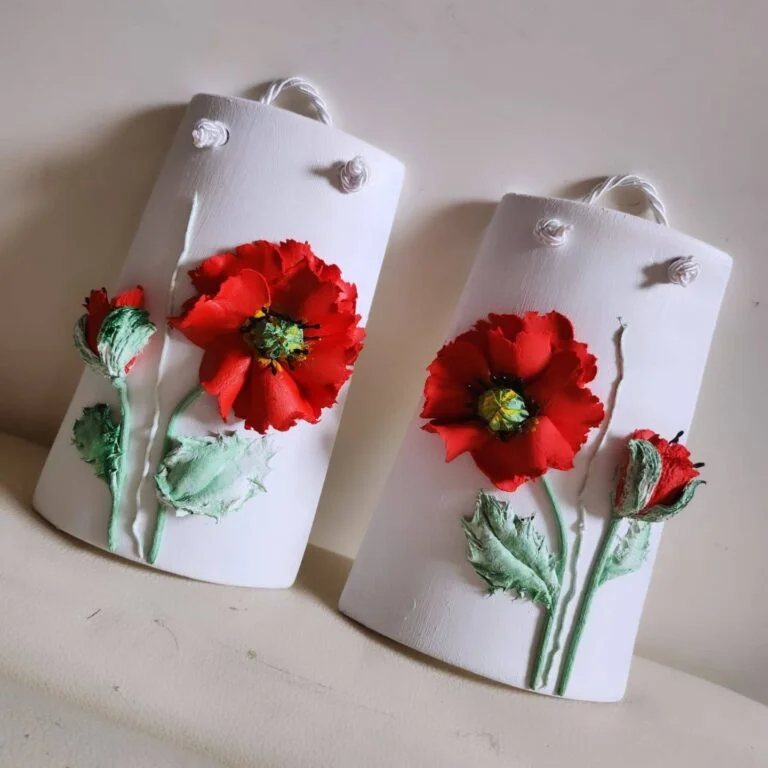 Collezioni Due targhe bianche appese, su cui sono raffigurati fiori di papavero rossi in 3D e foglie verdi, esposte su uno sfondo neutro.